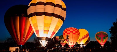 Baloane cu aer cald multicolore pe un câmp pe timp de noapte cu copaci în fundal