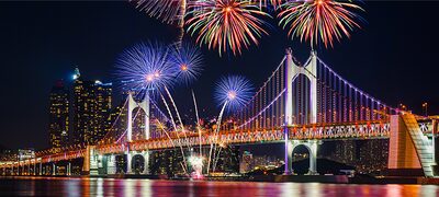 Focuri de artificii pe un cer de noapte peste un pod iluminat reflectat în râul de dedesubt
