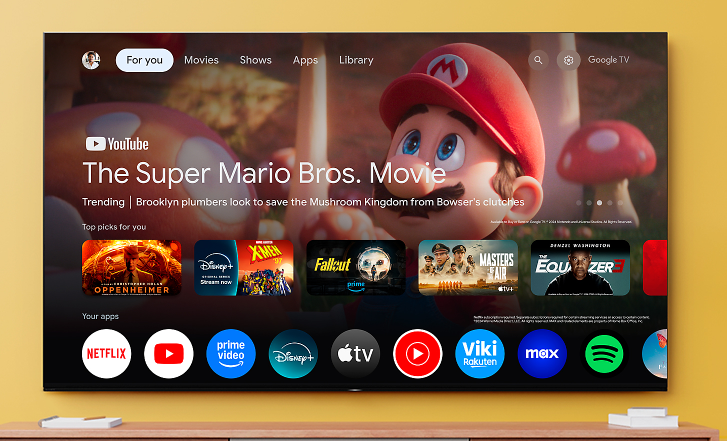 Televizor mare montat pe perete, afișând interfața Google TV, cu filmul The Super Mario Bros. Aplicații de streaming afișate dedesubt.