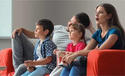 Bărbat și femeie cu doi copii pe canapea uitându-se la televizor