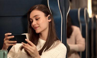 Imagine de stil de viaÅ£Ä cu o femeie folosind cÄÈtile WF-1000XM3 pentru a se bucura de conÅ£inut video pe smartphone.