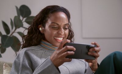Femeie stând într-o sufragerie purtând căștile LinkBuds S și urmărind un videoclip pe smartphone